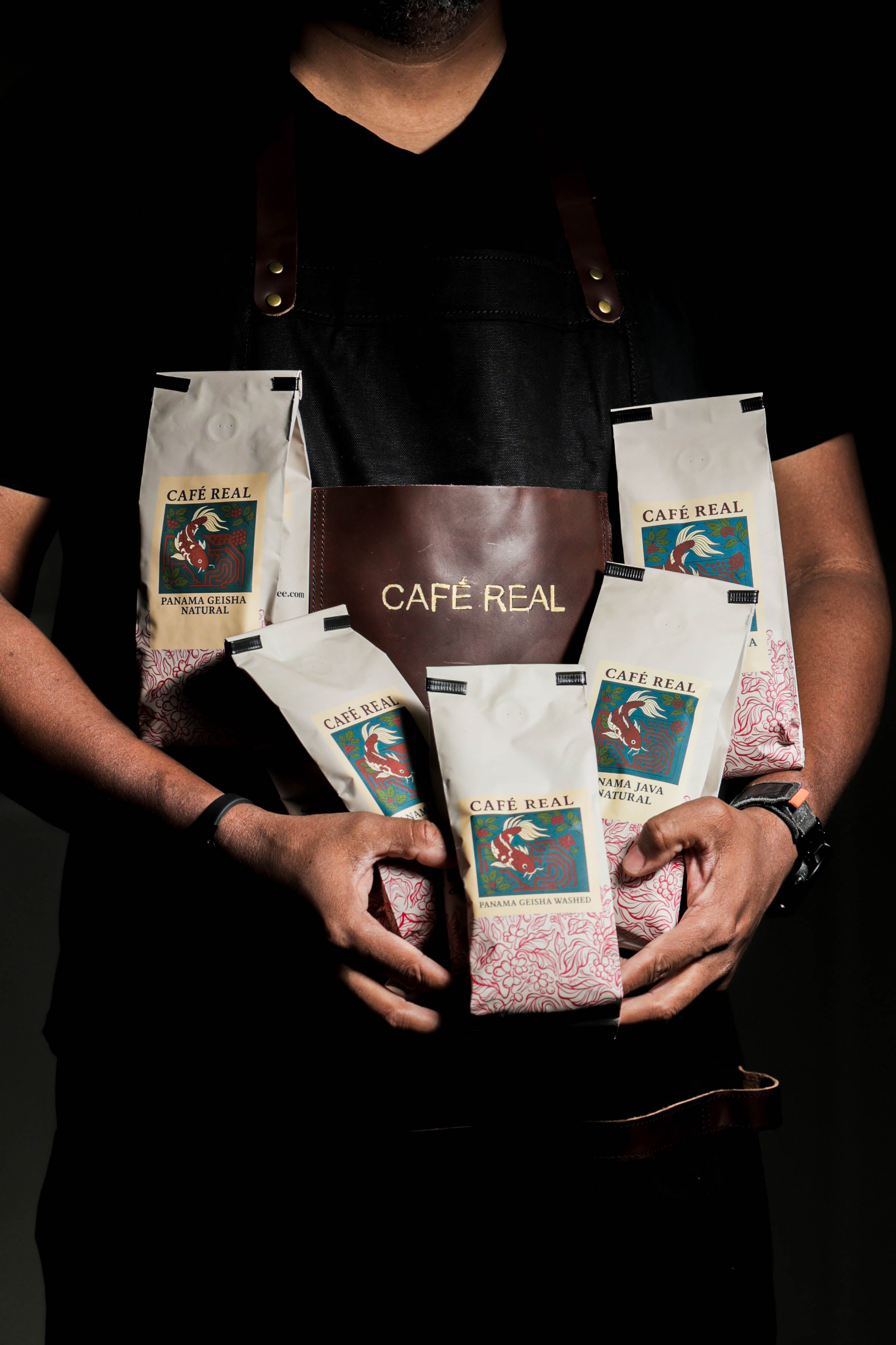 Person holding multiple Cafe Real coffee bags against a dark background